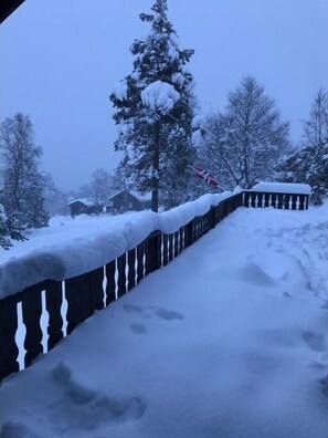 Et snedækket træhegn med gelænder, et snebelastet træ og et hus i baggrunden.