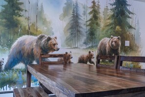 Une table à manger avec des chaises, placée devant une fresque représentant des ours dans une forêt.