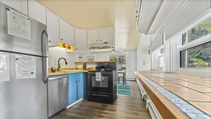A compact kitchen with a refrigerator, stove, and blue cabinets. - LOCATION~Walk 2 SeaLife&Parks~Perfect 4 Families (Seward)