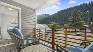 A wooden deck with wicker chairs and a view of a forested mountain. - The Wilders View | Downtown Seward · Deck Views · Sleeps 7 (Seward)