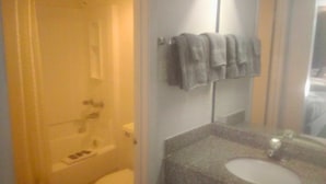A bathroom with a toilet, a sink, and a mirror. There are towels hanging on a rack.