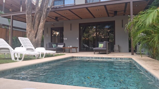 Una piscina con sillones de descanso y un área de patio cubierta.