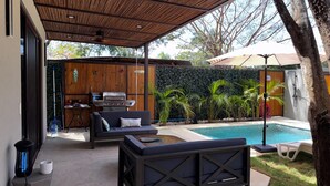 Un patio exterior con piscina, zona de barbacoa y mobiliario.