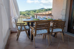 A terrace with a table set for two, wooden chairs, and a view of a hill. - Villa Jasmine Emerald (Sardegna)