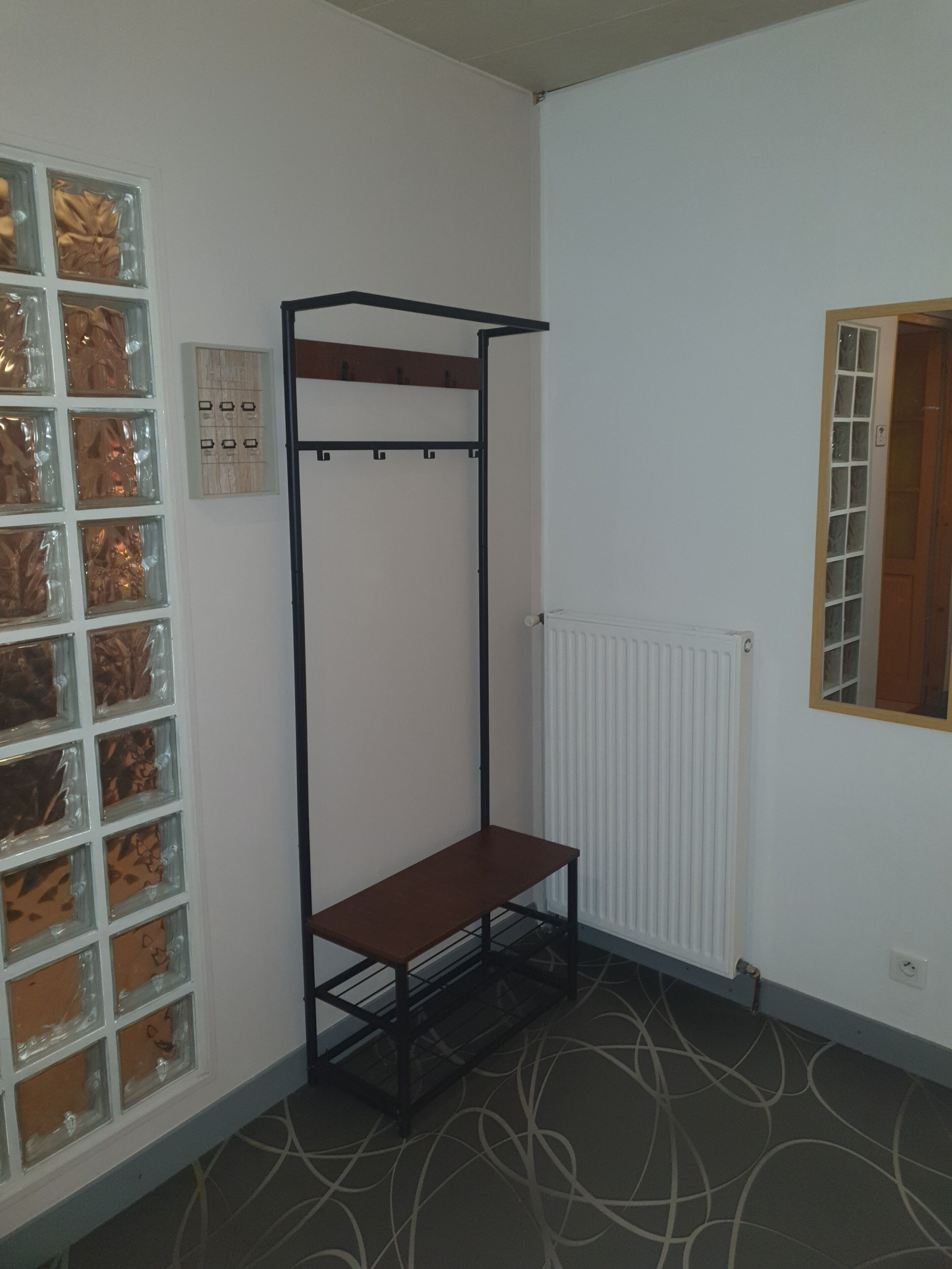 Huoneessa on metallinen hylly, patteri ja kuvioitu lattia.