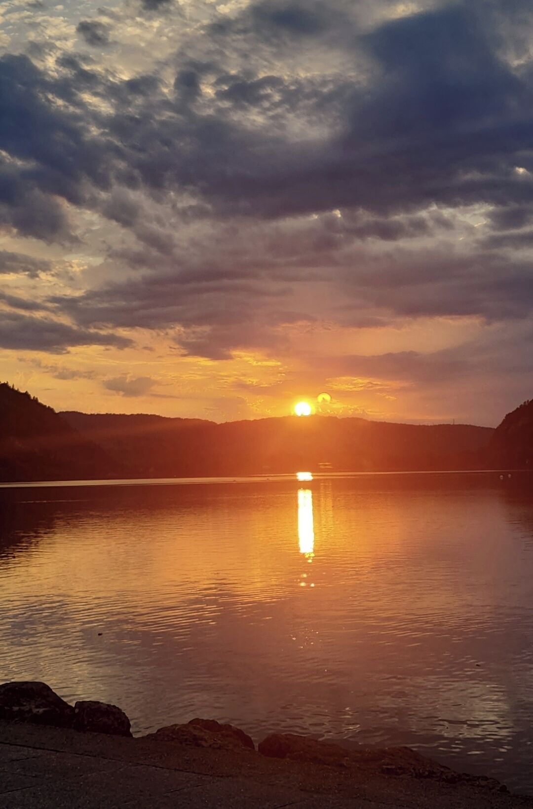 Un atardecer sobre un lago tranquilo con una cadena montañosa a lo lejos.