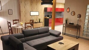 A modern living room with a sectional sofa, a wooden coffee table, and a dining area with a table and chairs. - 100m2 apartment between lakes and mountains (Nantua)