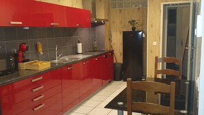 A modern kitchen with red cabinets, a black refrigerator, and a dining table with two chairs. - 100m2 apartment between lakes and mountains (Nantua)