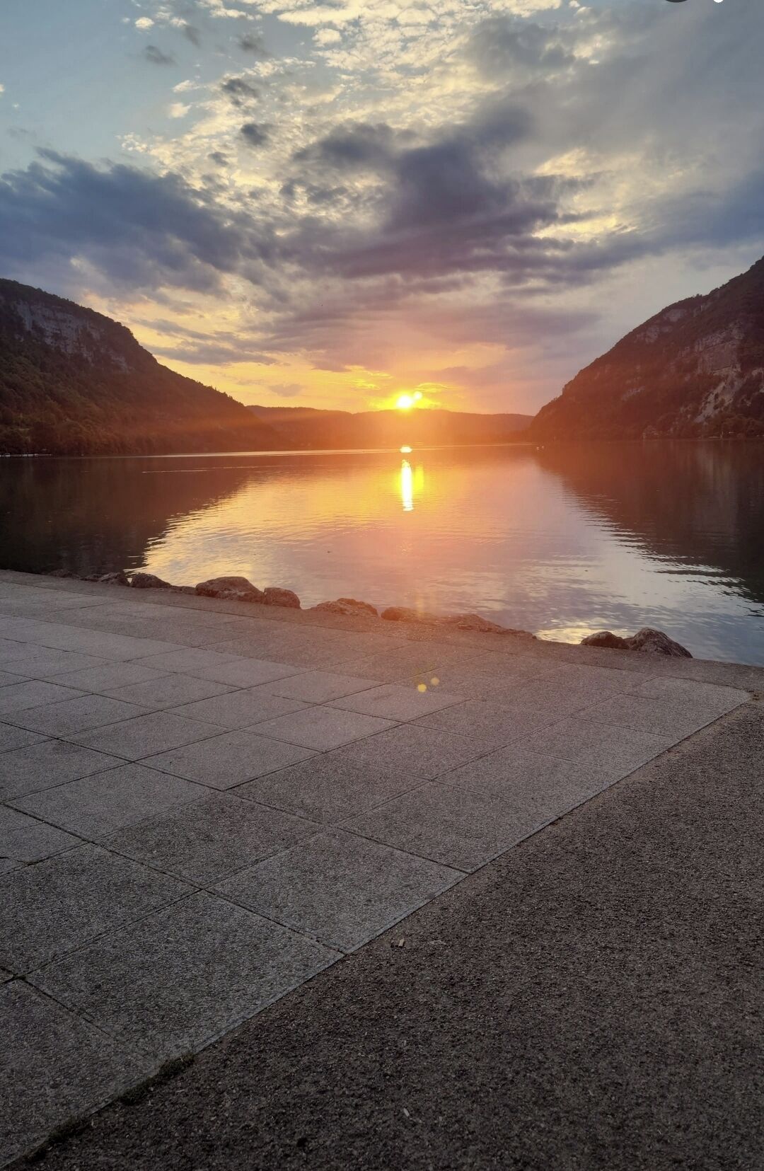 Ein friedlicher See mit Sonnenuntergang, ruhigem Wasser und einem gepflasterten Weg.