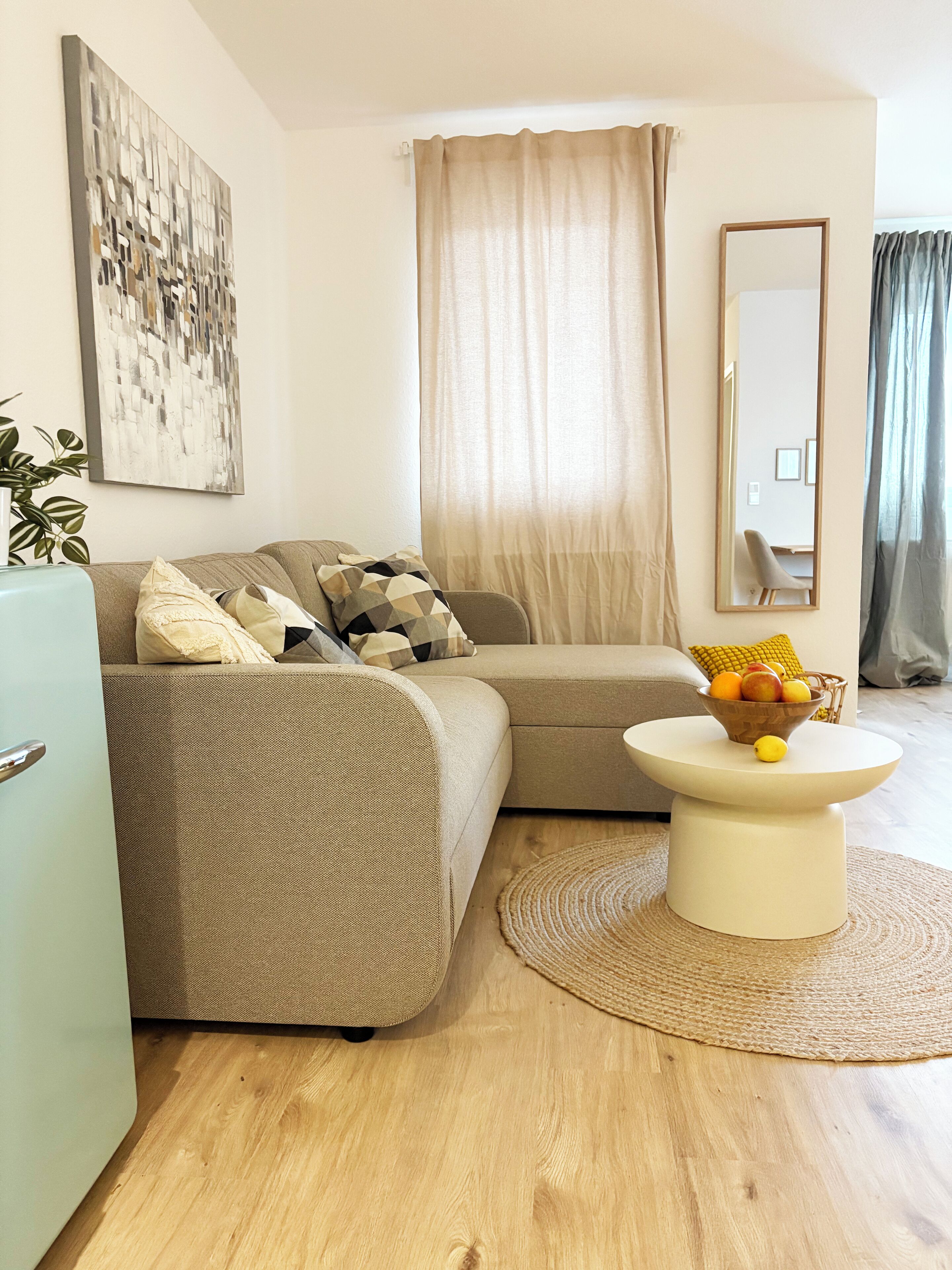 Una sala de estar moderna con un sofá color crema, una mesa redonda con fruta y un cuadro abstracto grande en la pared.