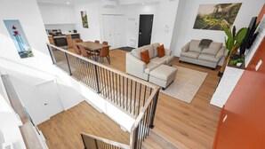 Eine moderne Wohnung mit einer Holztreppe, einem Essbereich, einem Wohnzimmer mit Sofa und Fernseher sowie einer Küche im Hintergrund.
