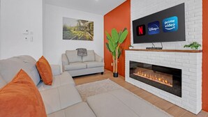 Ein modernes Wohnzimmer mit Kamin, einem Flachbildfernseher, der Streamingdienste anzeigt, und einer Sofagarnitur.
