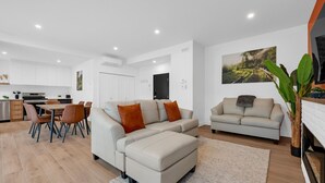 Ein modernes Wohnzimmer mit einer Couch, einem Essbereich mit Stühlen, einer Küche und einer großen Pflanze.