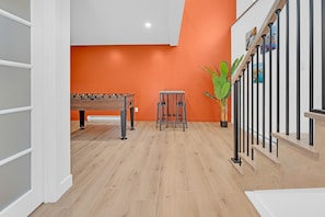 A room with a wooden floor, a foosball table, a bar stool, and a staircase with a railing. - Unit 102 - 2 Stories - 55" TV - Foosball - Downtown (Rimouski)