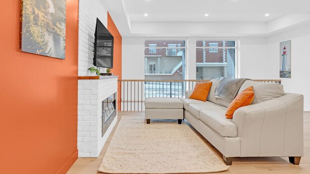 Una sala de estar moderna con chimenea, un sofá y vistas de edificios a través de amplios ventanales.