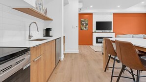 Una cocina moderna con lavavajillas, cafetera y televisión en la sala de estar, con una pared de acento naranja.