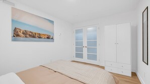 Un dormitorio con cama, armario, puerta con paneles de vidrio esmerilado y un cuadro enmarcado en la pared.