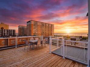 A wooden deck with outdoor seating and a view of a sunset over a cityscape. - Apartment 103 | NEW | Downtown (Rimouski)