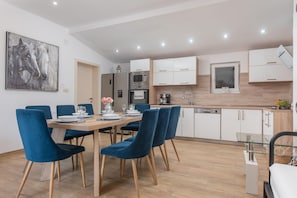 A modern kitchen with white cabinets, a microwave, and a dining area with blue chairs and a wooden table. - Peaceful Holiday Villa in Kladnjice (Lećevica)