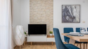 Een moderne woonkamer met een flatscreen televisie, een eettafel met stoelen, een metselwerk muur en een schilderij van paarden.