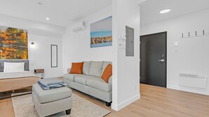 Une chambre moderne avec un lit, un canapé gris, une petite table et une grande fenêtre.
