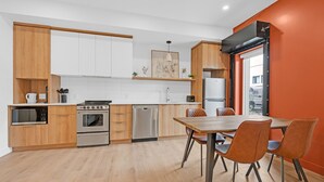 Une cuisine moderne avec des meubles en bois, des appareils électroménagers en acier inoxydable et un coin repas comprenant une table et des chaises.