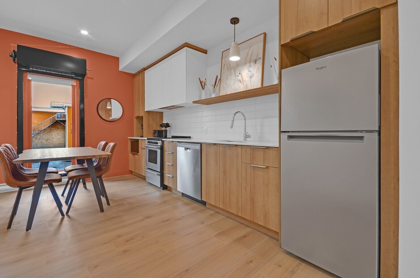 Una cocina moderna con armarios de madera, un refrigerador de acero inoxidable, lavavajillas y un comedor con mesa y sillas.