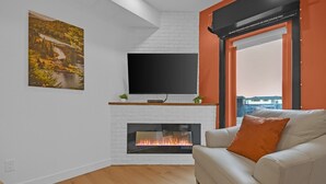 Olohuone, jossa on takka, televisio ja oranssi koristetyynyllä varustettu sohva.