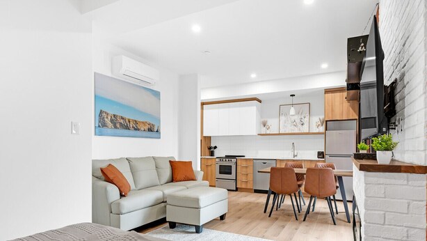 Ein modernes Wohnzimmer mit einer Couch, einem Essbereich mit Stühlen, einer Küche mit Schränken und Geräten sowie einem großen Gemälde an der Wand.