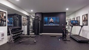Ein modernes Fitnessstudio mit Trainingsgeräten, Laufband und Fernsehbildschirm, der Trainingsvideos zeigt.