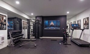 Un gimnasio moderno con equipo de ejercicio, una cinta de correr y una pantalla de televisión que muestra videos de entrenamiento.