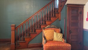 A staircase with wooden railings and a chair with patterned upholstery. - Victorian home built in 1834. (Union City)