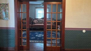 A room with a wooden door leading to another room with a patterned rug and a sofa. - Victorian home built in 1834. (Union City)