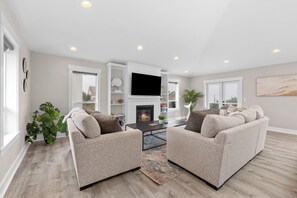 A modern living room with a fireplace, two sofas, a coffee table, and a flat-screen TV. - Ocean View • Hot Tub • Three Floors • Sleeps 10 • Olivia Beach Family Getaway (Lincoln City)