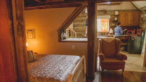 A cozy bedroom with a bed, a chair, and a view into a kitchen area. - Moonshine Runners Cabin (Tracy City)