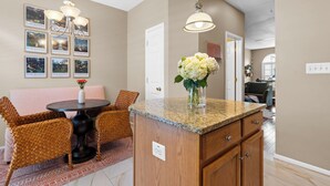 Una cocina con encimera de granito, armarios de madera, comedor con sillas de mimbre y una lámpara colgante.