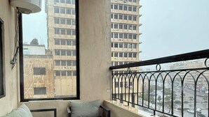 Un balcón con sofá, sillas y una mesa. Se ve una vista de edificios altos y una calle abajo.