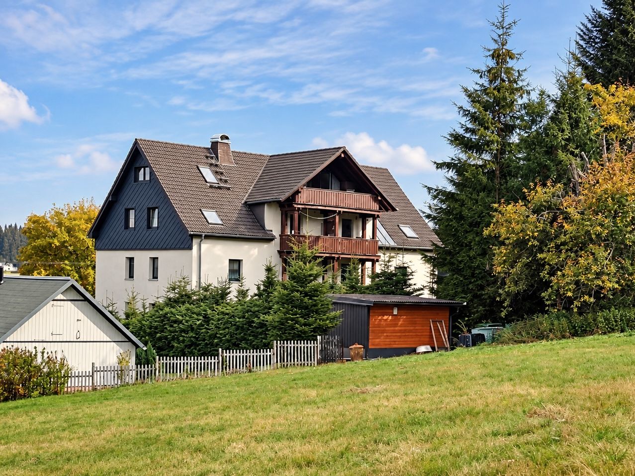 A two-story house with a sloped roof, a balcony, and a fenced yard.