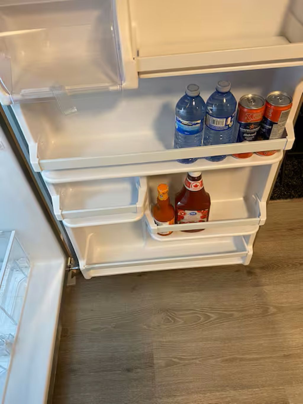 An open refrigerator with water bottles, a bottle of ketchup, and a can of soda.