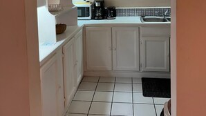 Una cucina con mobili bianchi, un forno a microonde, una macchina del caffè e una sveglia appesa al muro.