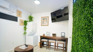 A modern room with a wooden dining table, three chairs, a TV mounted on the wall, and a green wall. - Your Calm Escape  Modern Guesthouse ADU Sanctuary (San Bernardino)