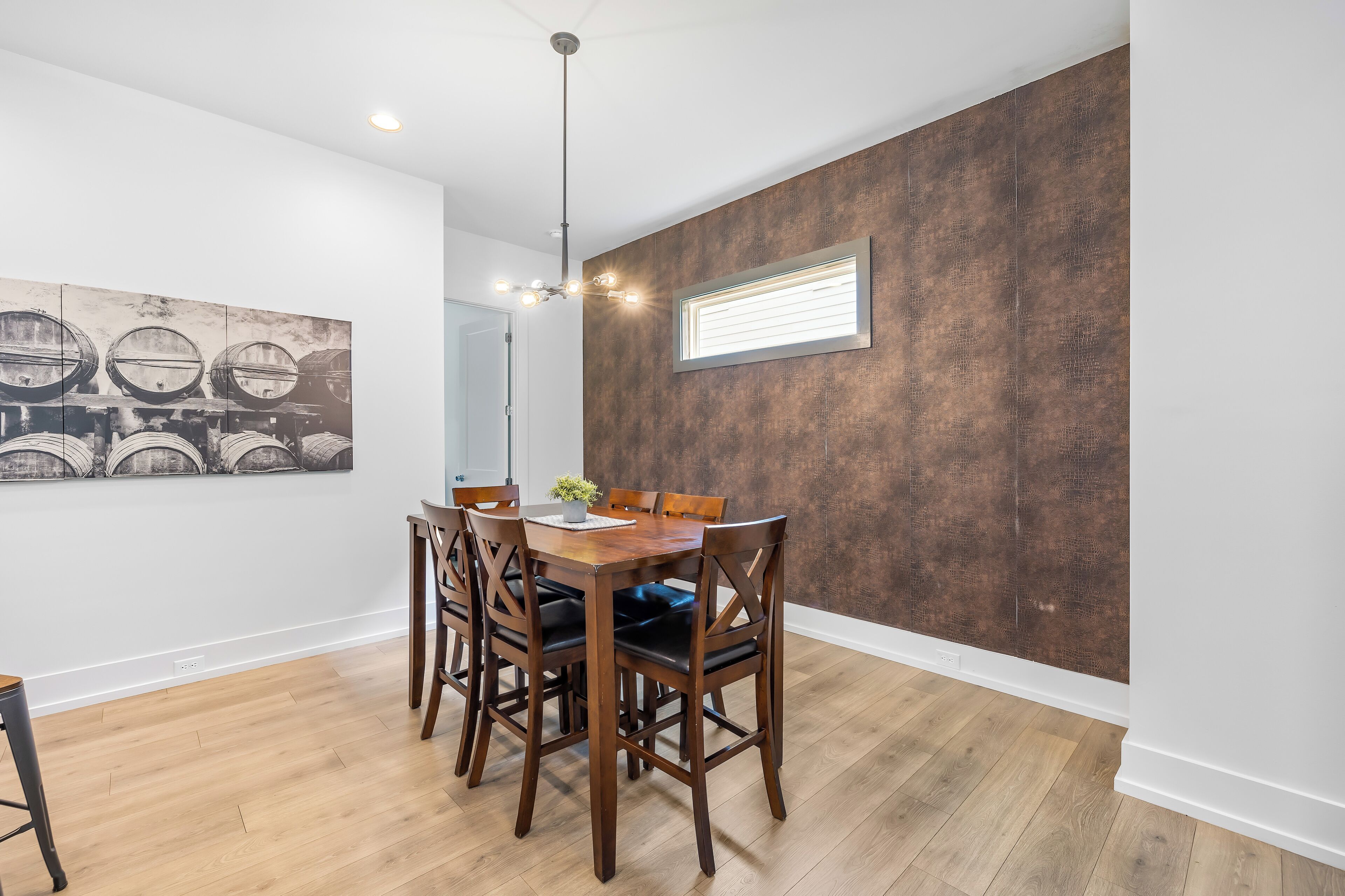 A dining area with a wooden table and chairs, a ceiling light fixture, and a large abstract painting on the wall.