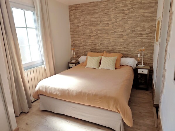 Un dormitorio con una cama grande, dos mesitas de noche, una ventana con cortinas y una pared con diseño de ladrillo.