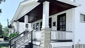 A two-story house with a porch, a staircase, and a stone foundation. - Updated Home: Min From Airport: Cozy Duplex Unit (Cleveland)