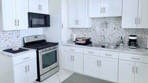 A modern kitchen with white cabinets, a stainless steel stove, a microwave, a sink, and a coffee maker. - Updated Home: Min From Airport: Cozy Duplex Unit (Cleveland)