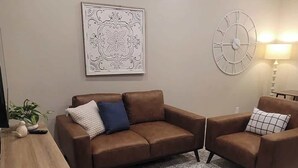 Una sala moderna con un sofá de cuero marrón, un tapete estampado, un reloj de pared y una mesa con una lámpara.