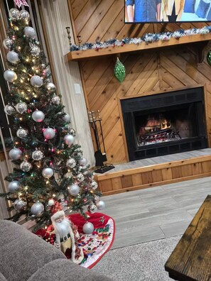 A cozy living room with a large Christmas tree, a fireplace, and a television mounted on the wall. - Fully Renovated Mountain House with a Private Spa (Lake Harmony)
