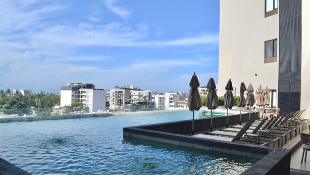 Ein Poolbereich mit Liegestühlen und Sonnenschirmen mit Blick auf einen Strand und Gebäude.