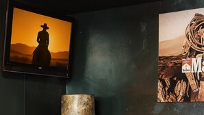 A room with a dark green wall, a brown sofa, a framed picture, a lamp, and a suitcase.