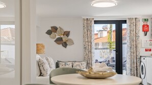 Uma sala de estar moderna com um sofá, uma mesa de jantar com uma tigela, um objeto decorativo na parede e vista para o exterior através de uma porta.